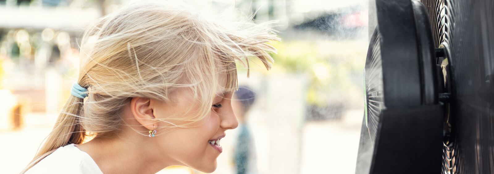 Profile Side Close Up View Cute Little Blond Kid Enjoying Fresh Moisturized Air Blowing From Big Cooling Fan Machine Hot Sunny Summer Weather Outdoors. Mist Spraying Ventilator System Phoenix, Arizona